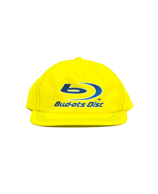 A bright yellow Snapbackcap featuring a blue and white Bud-ots Disc logo embroidered on the front, set against a plain white background.